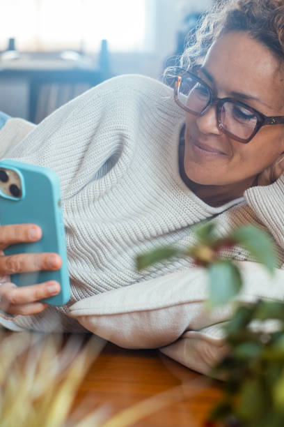 istock One modern middle age woman scrolling and writing on smart mobile phone alone at home in relaxation indoor leisure activity laying on the floor and smiling at the display device. Using cell app 2154623175