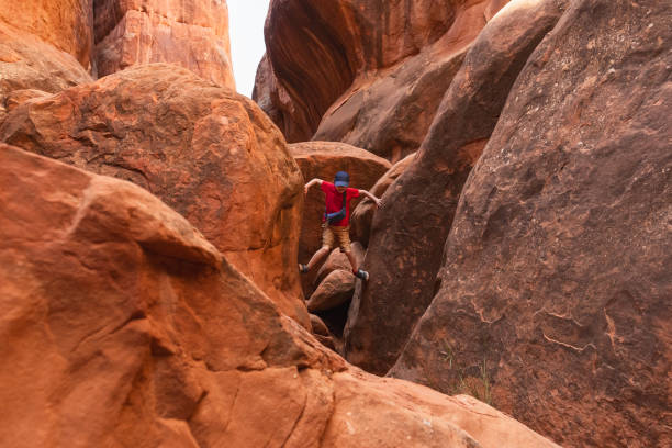 Young Hiker Boy Climbing through the Narrow Path in Fiery Furnace in Arches National Park, Utah, United States.