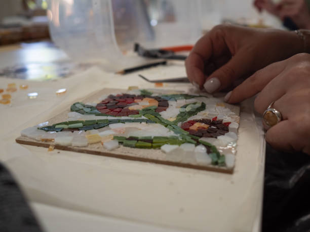 istock Mosaic Workshop: A horizontal tabletop close-up shot captures a woman's hands crafting a floral mosaic pattern. 2154630472