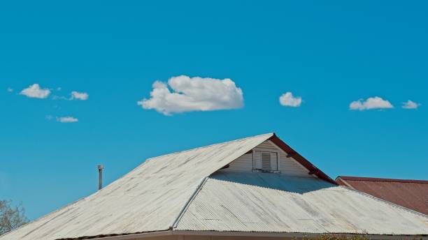 Tin metal roofline against bright blue sky and cumulus clouds. Design element with copy space.