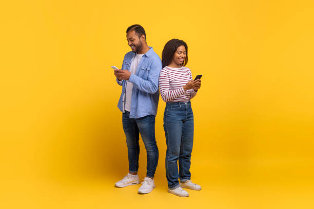 istock Two People Standing Back-to-Back Using Smartphones Against a Yellow Background 2154637887