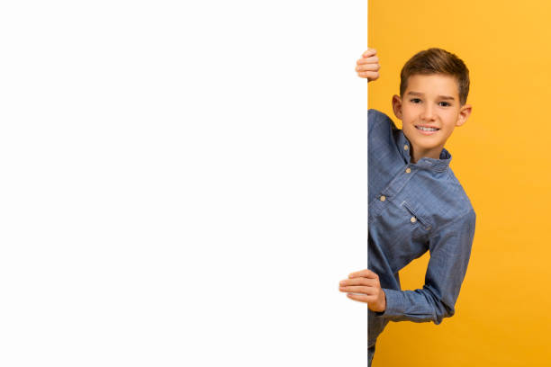 istock Cheerful teenage boy peeping from behind a blank white advertisement board 2154643344