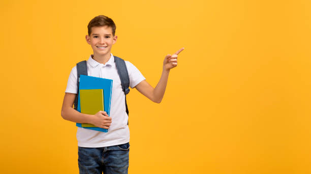 istock Happy schoolboy carrying backpack and textbooks and pointing aside at copy space 2154643355