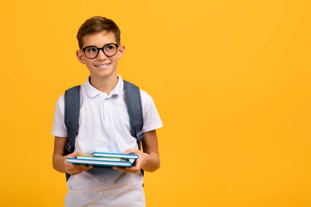 istock Intelligent schoolboy wearing glasses and backpack holding textbooks and looking aside 2154643367