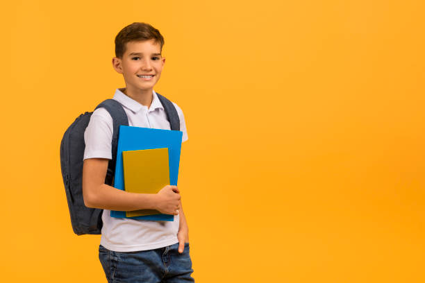 istock Smiling schoolboy carrying backpack and textbooks standing against yellow studio background 2154643399