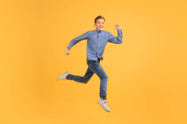 Dynamic teen boy jumping in air against yellow studio background, happy male teenager radiating joy and energy, encapsulating the essence of freedom and happiness in youth, copy space