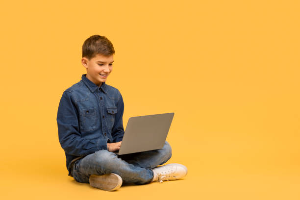 istock Smiling teenage boy sitting cross-legged on floor and using laptop 2154643487
