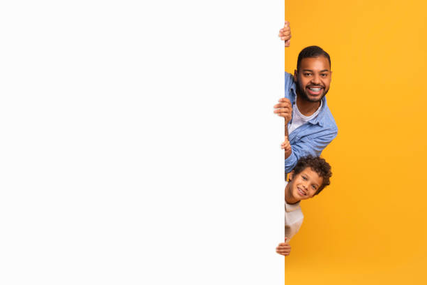istock Black Father And Son Peeking Out Of Blank Advertisement Board 2154645082