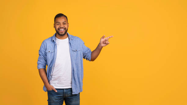 istock Joyful young black man pointing aside at copy space on yellow background 2154645091