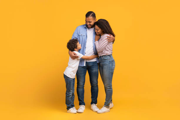 istock Little black boy embracing his parents while they standing on yellow background 2154645098