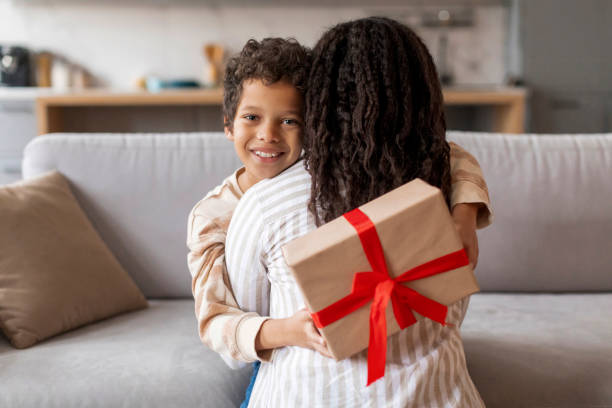 istock Little black boy presenting surprise wrapped gift to his mother 2154646391