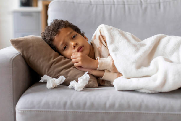 istock Ill little black boy resting under blanket on couch at home 2154646398