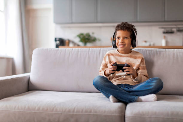 istock Cheerful black boy wearing wireless headphones playing with game controller 2154646403