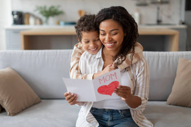istock Smiling black mother reading handmade heart card from her cheerful son 2154646433