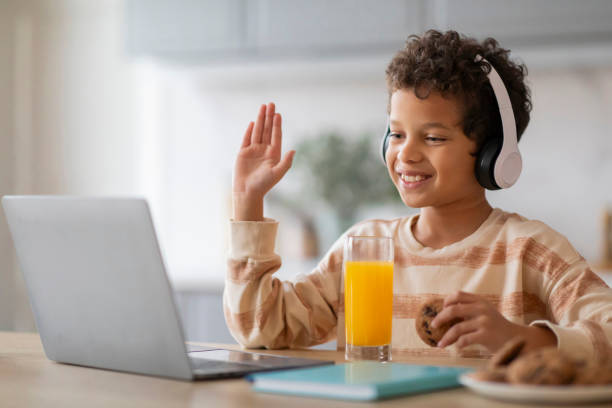 istock Cheerful black boy wearing headphones participating in virtual class on laptop 2154646435