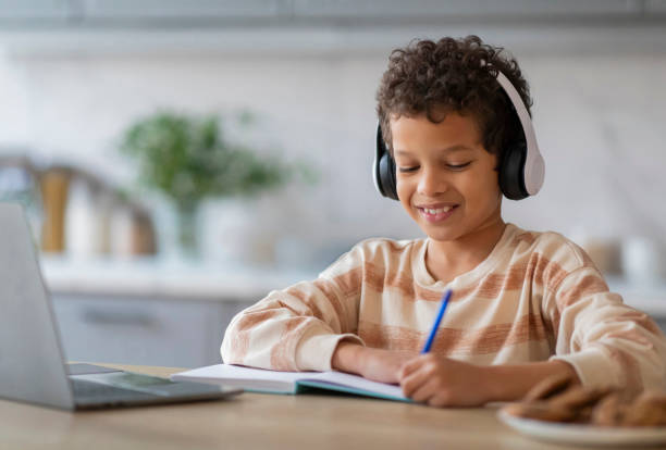 istock Online Lesson. Black Boy In Wireless Headphones Study With Laptop At Home 2154646449