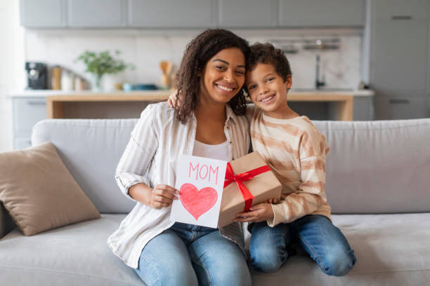 istock Mother's Day Gift. Black boy greeting mom with handmade card and present 2154646527