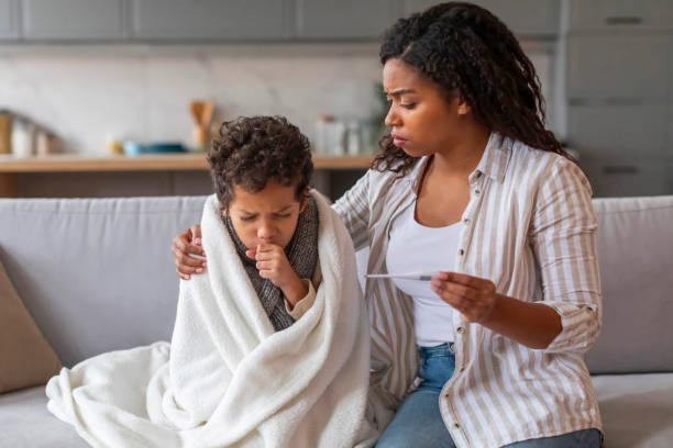 Worried black mother holding thermometer and looking at her coughing son Worried black mother holding thermometer and looking at her coughing son wrapped in blanket, african american mom taking care about male child during sickness, sitting on couch in home environment young hot stock pictures, royalty-free photos & images