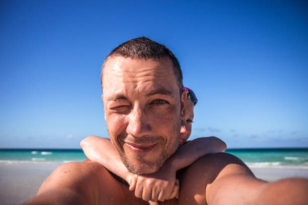 Daughter hugging his father playing piggy back on the beach during summer vacation