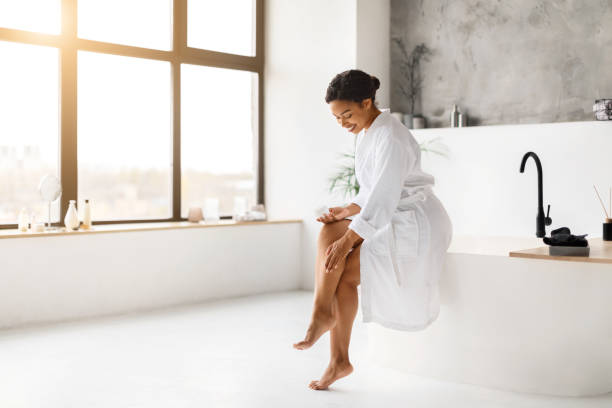 istock Happy African American Lady Applying Moisturizer Cream On Legs In Bathroom 2154649464