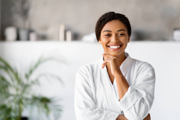 istock Attractive young black woman in white bathrobe standing in bathroom 2154649498