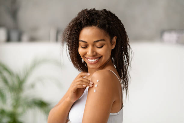 istock Joyful black woman smiling while applying body lotion to her shoulder 2154649499