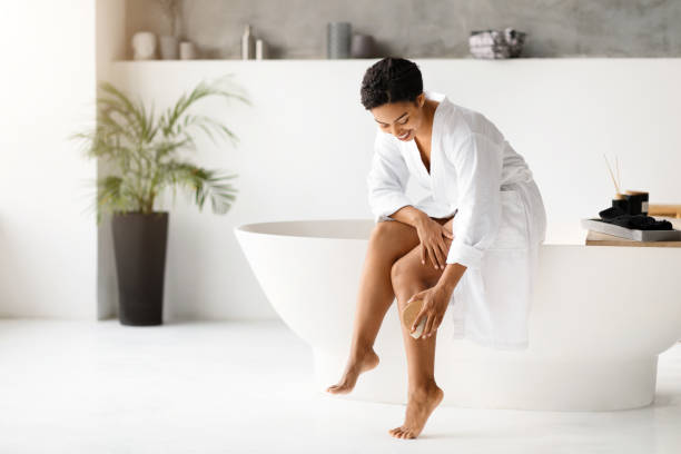 istock Smiling black woman in bathrobe dry brushing legs, practicing skin exfoliation routine 2154649502