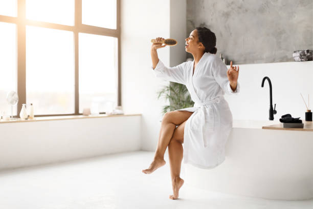 istock Delighted black woman in bathrobe using hairbrush as microphone, singing and dancing 2154649517