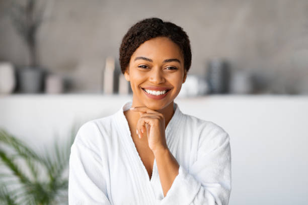istock Beautiful young black woman wearing bathrobe touching face and smiling at camera 2154649540