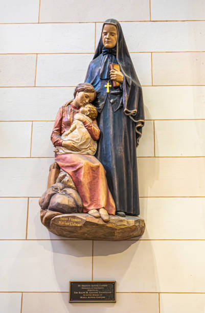 New York, NY, USA - August 2, 2023: Saint Frances Xavier Cabrini small statue set against white wall. Has her hand on young mother and child