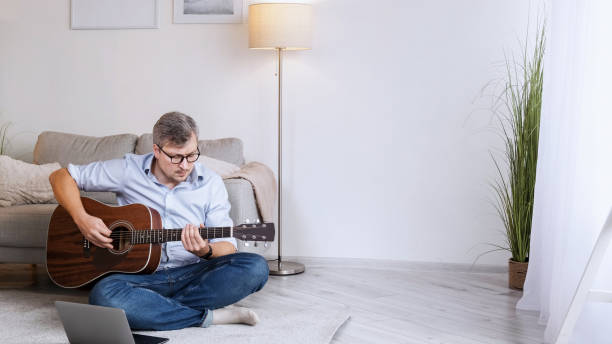 istock Guitar class video lesson man laptop floor home 2154664285