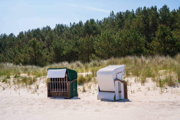 On the sandy beach there are two strandkorbs facing in different directions. Protection from wind and sun. Baltic Sea, Germany.
