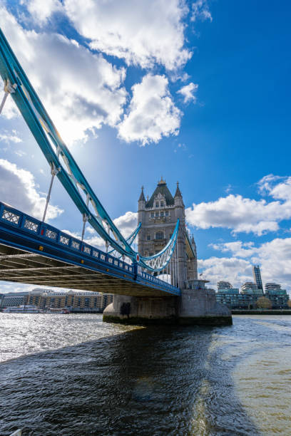 istock Diagonal view from below of London's Tower Bridge casting its shadow on the River Thames under a blue sky with white clouds backlit by the morning sun. 2154696652