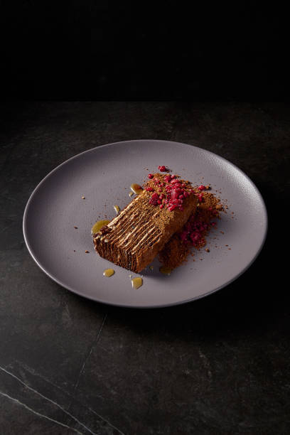 Vertical side perspective of a Medovik honey cake complemented by raspberries, elegantly placed on a gray plate with a contrasting dark ambiance