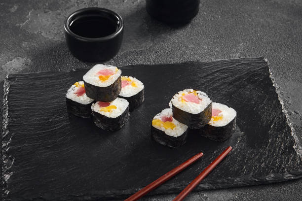 istock Delicate maki sushi rolls filled with fresh tuna and sweet mango, artfully displayed on a black slate with soy sauce on the side 2154701952