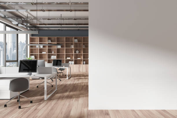 istock Modern office interior with desks, computers, and city view, featuring a wooden floor and bookshelf, with an empty wall mockup. 3D Rendering 2154703256