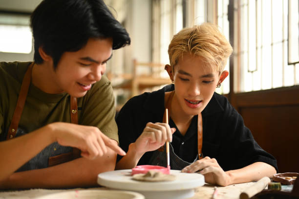 Two students are joyfully collaborating in an art class, painting a ceramic piece together. The image captures their engagement and teamwork in a creative environment