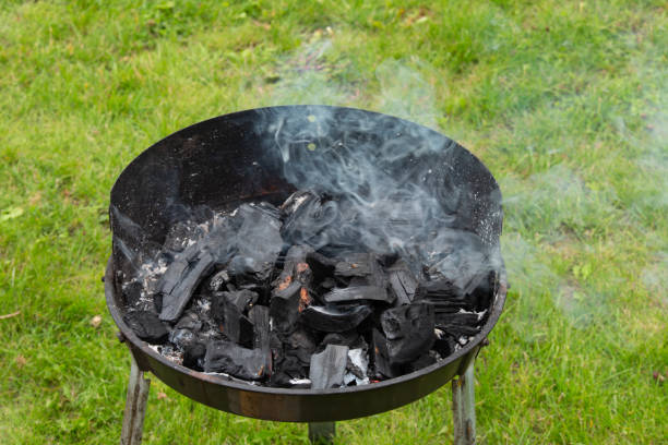 metal grill on a sunny spring day, green grass smoking with black coals