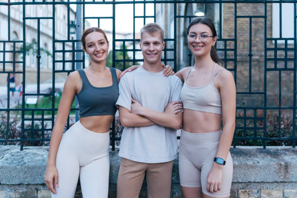 A group of three young friends, showcasing the positivity and vitality associated with city life, stand casually in an angular pose, sharing a moment of happiness and friendship while exuding the healthy lifestyle of sports enthusiasts The outdoor setting accentuates the concept of real people enjoying a recreational pursuit together, embodying the spirit of togetherness and wellbeing