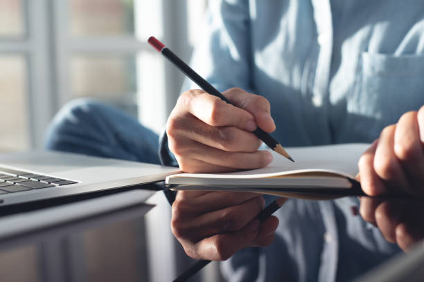 istock Woman hand with pencil writing on notebook with laptop computer on office table. Student studying online class and taking note, e-learning, business event planning, to do list reminder 2154707701