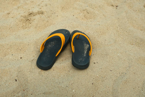 The image displays a single, dark blue flip-flop lying on a sandy surface.
