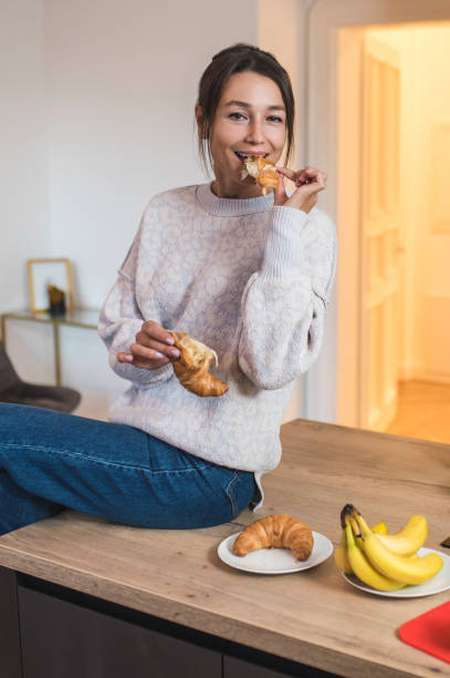 istock Young woman having breakfast at the kitchen and looking enjoyed 2154725892