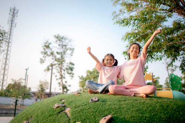 Brothers and sisters are running around and rolling on grass in a public park