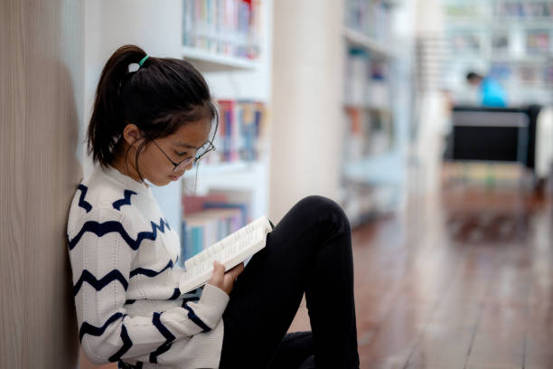 istock A girl is sitting on the floor reading a book 2154730361