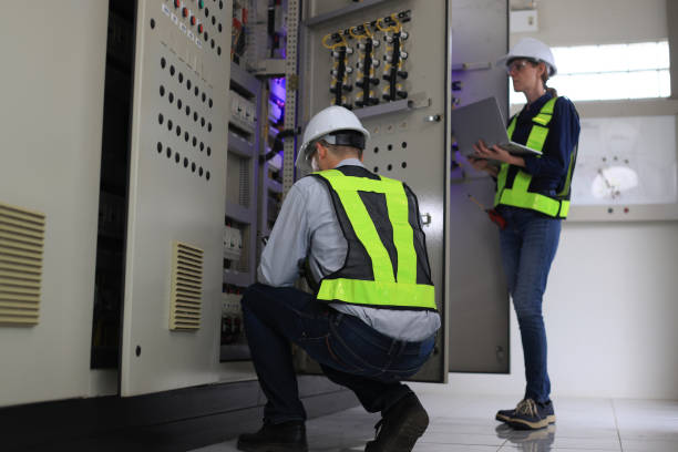 Two Caucasian white professional electrician engineers working with a computer and digital tablet in the main electric control room of the factory, MDB Main Distribution Board