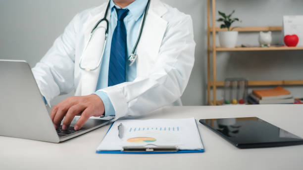 istock Male doctor sitting at work desk checking work plans and writing document reports in hospital office, healthcare worker and doctor service, digital laptop in modern office, medical technology concept. 2154739758