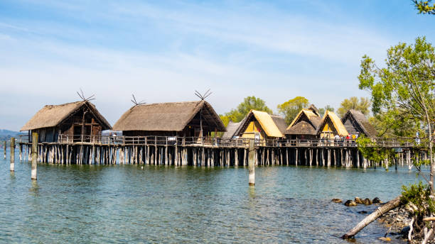 Cozy wooden houses on stilts overlook tranquil waters at a lakeside location. The warm hues from the sunset enhance the serene atmosphere, inviting relaxation.
