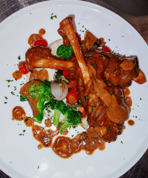 istock Braised lamb shank in restaurant. Modern style traditional braised slow cooked lamb shank in red wine sauce with shallots and mashed potatoes offered as top view with copy space. 2154755892