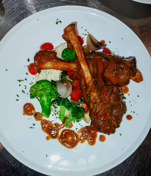 istock Braised lamb shank in restaurant. Modern style traditional braised slow cooked lamb shank in red wine sauce with shallots and mashed potatoes offered as top view with copy space. 2154755900