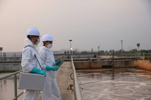 istock scientist and safety  engineer wearing chemical PPE protection work at wastewater treatment plant with tablets and survey patrol  on the  wastewater tanks 2154756773